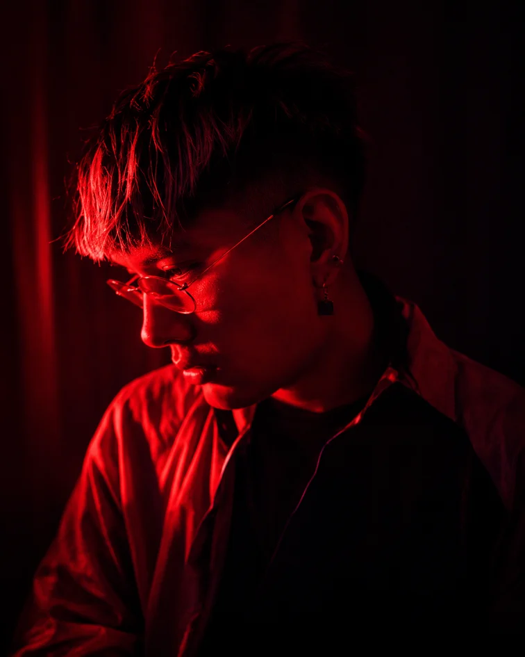 CLIFF de perfil bajo luz roja, con lentes de marco fino y una argolla en la oreja